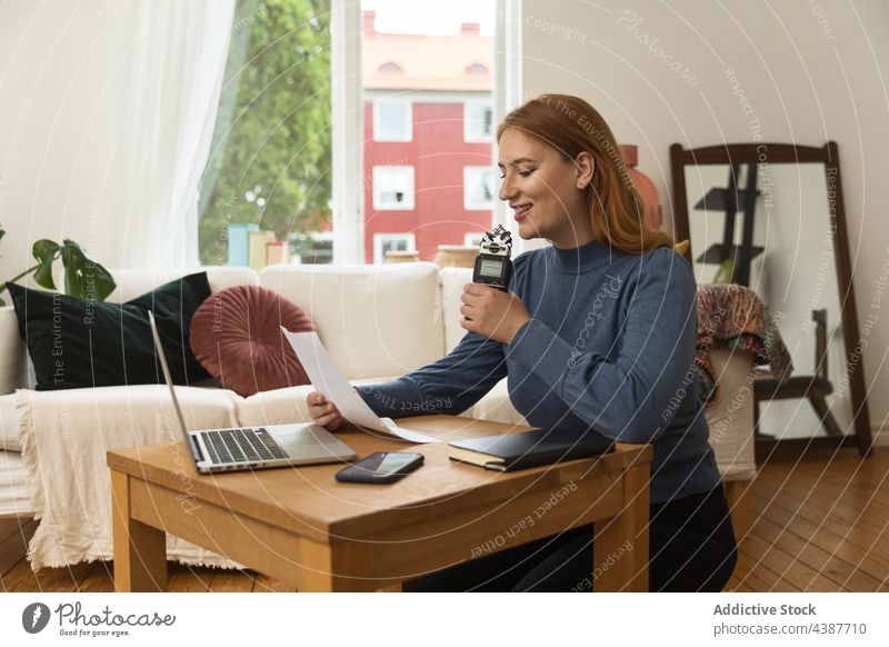 Cheerful woman recording podcast and using microphone speak talk headphones host radio female read note paper broadcast smile cheerful delight content home