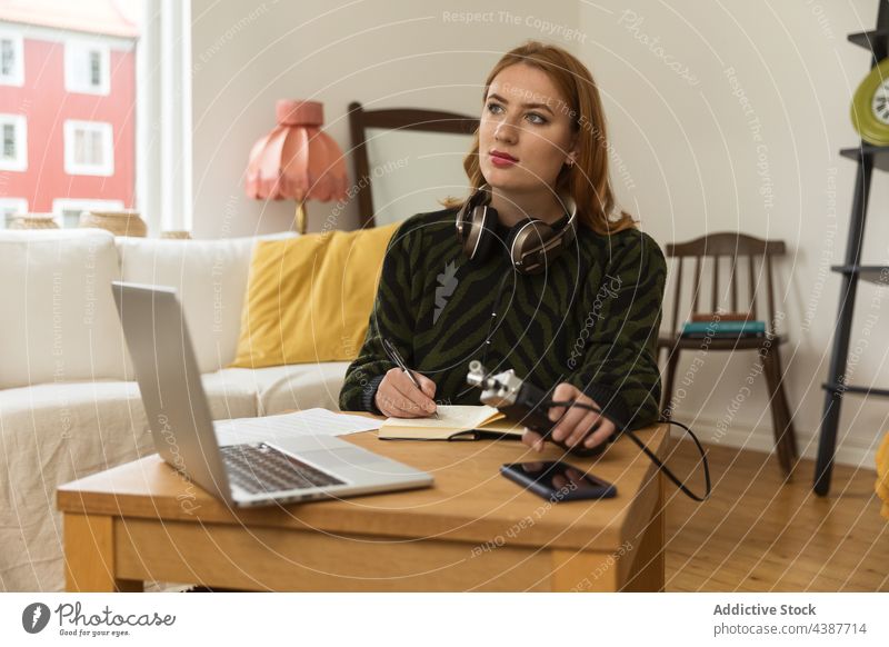 Pensive woman taking notes and preparing for recording podcast radio host prepare write take note notebook microphone female headphones broadcast laptop home