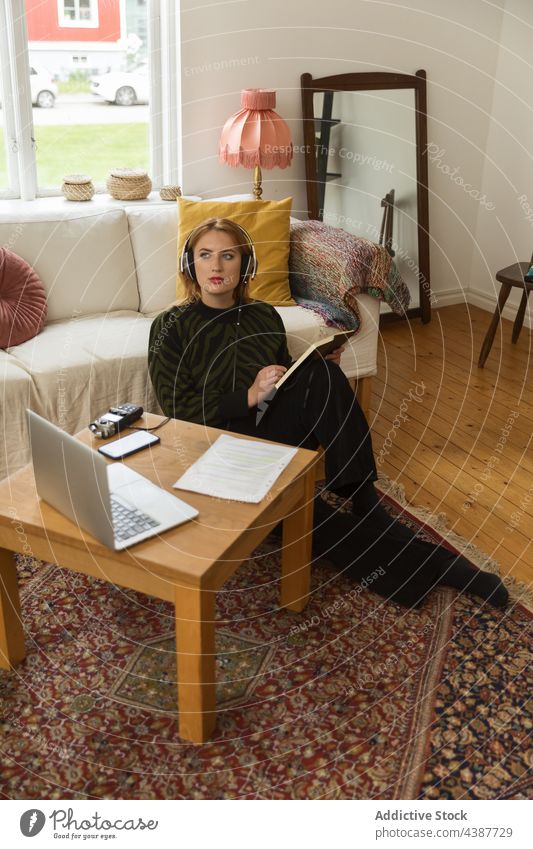 Woman in headphones taking notes and recording podcast woman radio host take note write notebook concentrate thoughtful female home floor sit notepad serious