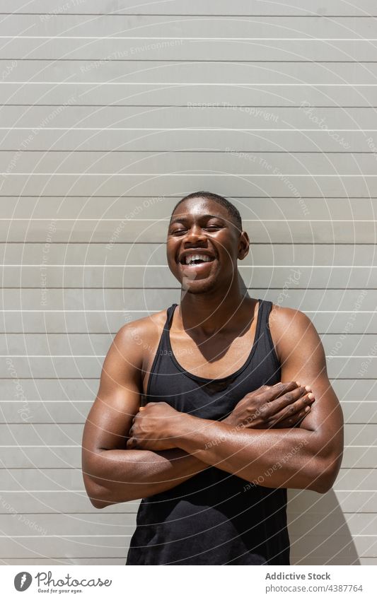 Black man laughing near wall in city cheerful fit strong summer sunny street delight positive male ethnic black african american sunlight summertime having fun