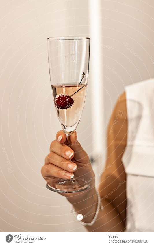 Elegant female hand with a french manicure holds a glass of champagne or rose sparkling wine. Human hands. Holiday or event concept. Vertical shot elegant
