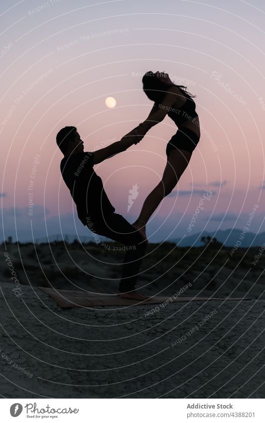 Silhouette of couple doing acroyoga against sunset sky acro yoga balance partner silhouette together practice acrobatic holding hands pose support sundown