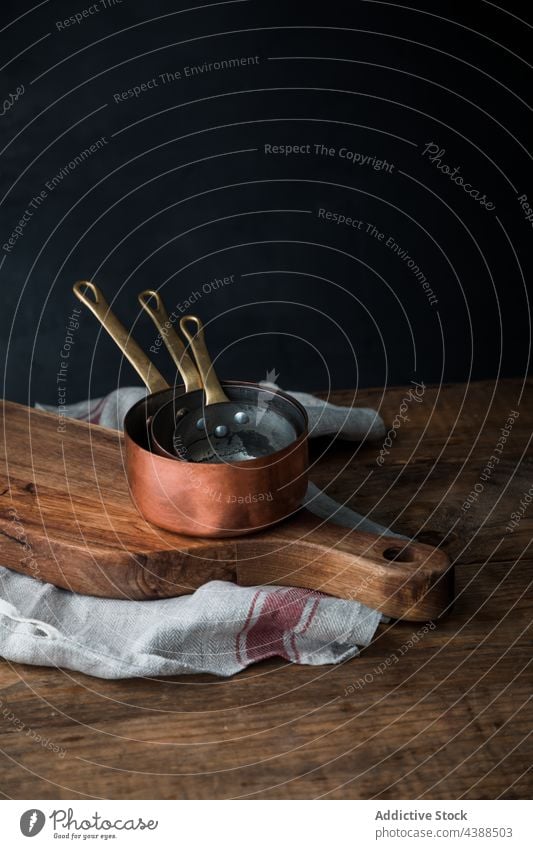 Set of copper saucepans on table cutting board towel rustic set composition wooden linen stack dark kitchen napkin shabby timber lumber metal cloth fabric