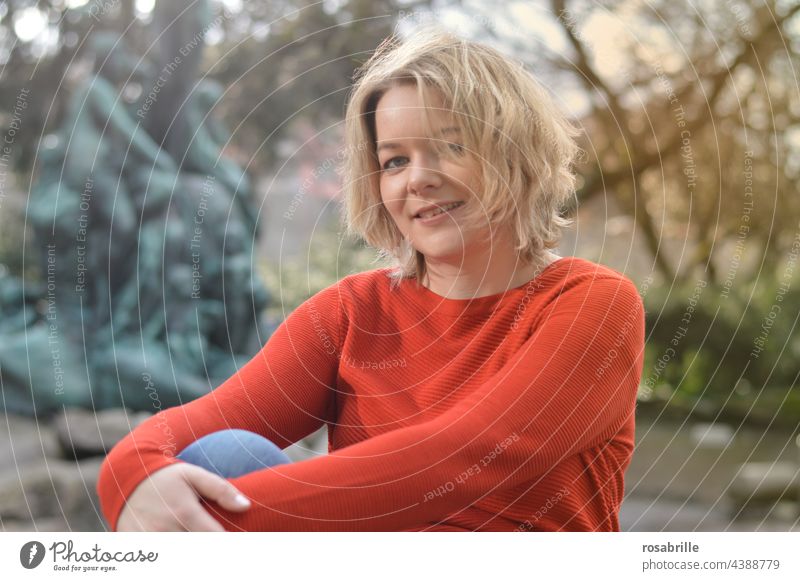 likeable young blonde woman in orange sweater smiling in the park Woman youthful Blonde Smiling Congenial naturally Authentic portrait Happiness Attractive