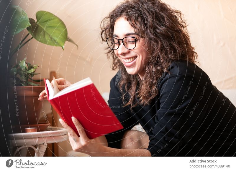 Young smiling woman in eyeglasses reading book hobby story free time literature study knowledge young curly hair hispanic ethnic eyewear spectacle female novel