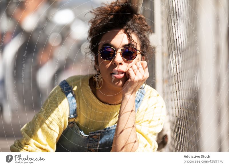 Stylish young woman in sunglasses style trendy fashion accessory modern urban sunlight millennial female lean hand eyewear denim yellow curly hair hispanic