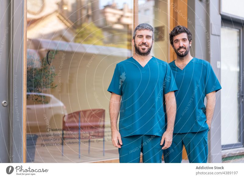 Cheerful doctors in uniform standing near clinic on street men together practitioner hospital building entrance cheerful colleague male coworker smile job