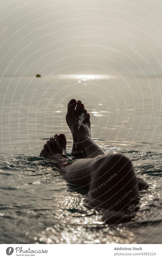 Crop anonymous woman lying in sea water in morning sunlight vacation tender early barefoot female playa de muro alcudia mallorca spain enjoy tranquil summer