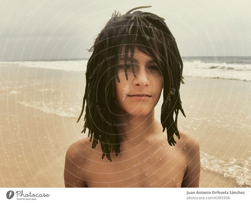 Close up portrait of a boy on the beach wearing a wig made from seaweed 12 year bizarre summer kid youngster man caucasian leisure creativity teen teenager