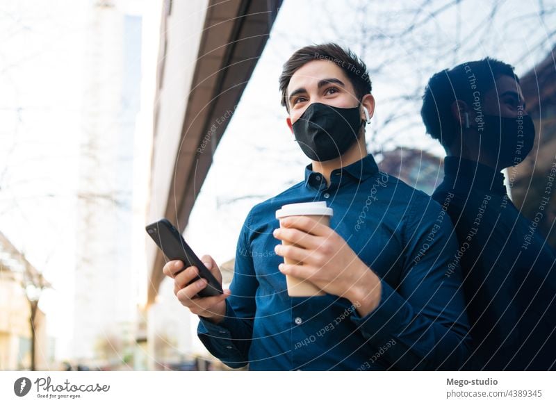 Young man using his mobile phone outdoors. young urban face mask covid-19 connection protection coffee portrait wireless telephone holding cup of coffee