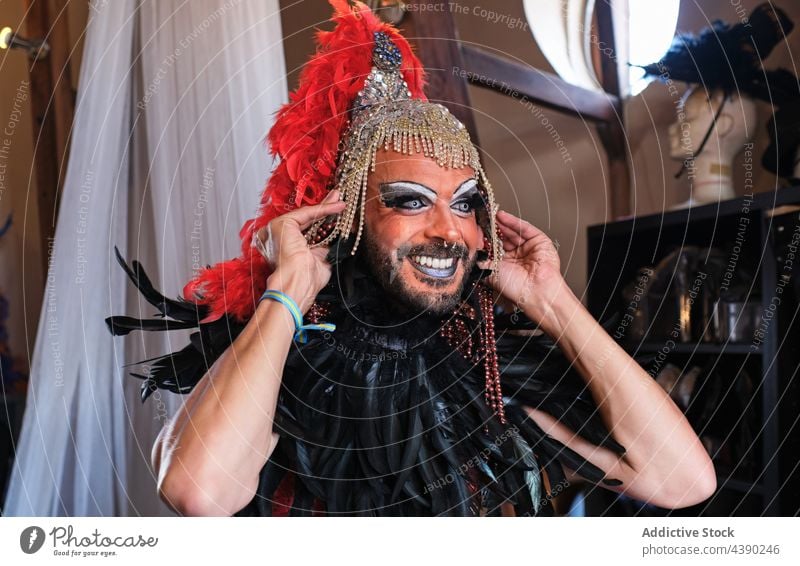 Bearded man in drag queen costume makeup outfit headdress smile wear gender accessory feather headwear headgear bracelet pride transgender feminine cloth