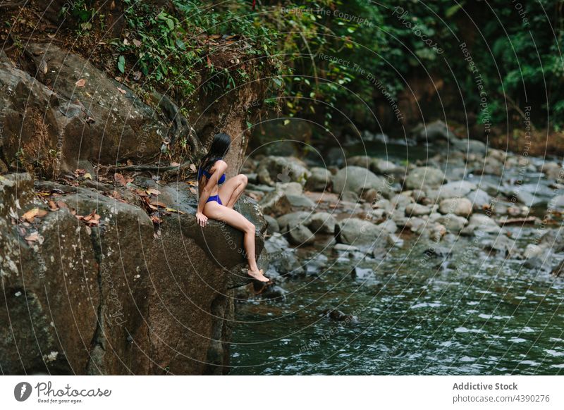 Woman sitting near river in forest woman rock nature traveler water stone relax alone female tourist vacation journey recreation costa rica alajuela la fortuna