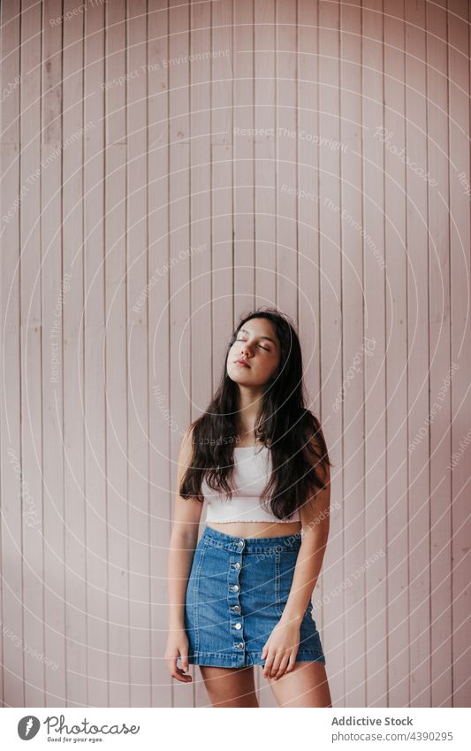 Young woman with eyes closed standing near wall dreamy calm teenage tranquil pensive brunette alone peaceful young female millennial denim crop top style casual