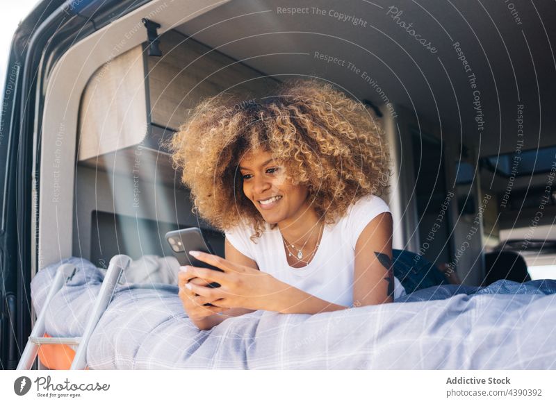 Cheerful black woman using smartphone on camper bed caravan road trip smile rest weekend summer vacation female young browsing cheerful ethnic african american