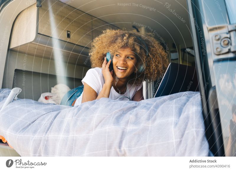 Black woman using netbook and listening to music in trailer laptop bed caravan tourism distant smile social media road trip female happy rest young weekend