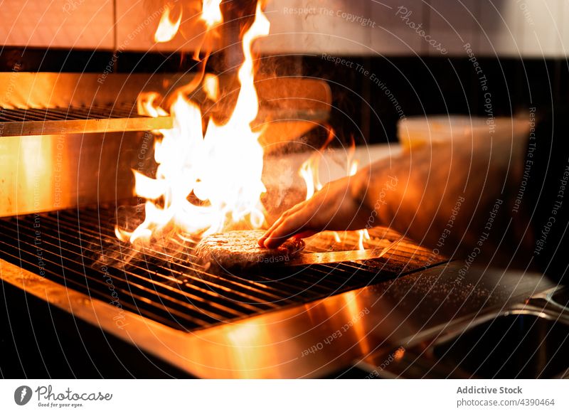 Crop cook grilling patty on grill in kitchen chef burger flame fire man prepare restaurant male food meal delicious tasty culinary hot meat heat burn cuisine