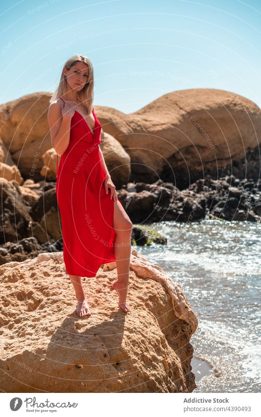 Woman in red dress on seashore woman beach rocky style summer fashion color female young blond barefoot outfit look sundress ocean coast nature seaside lady