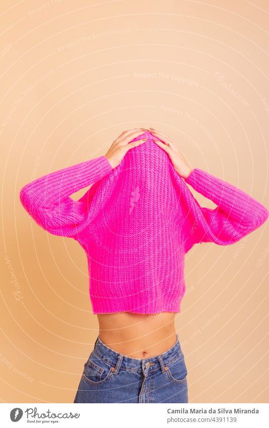 Portrait of girl with her trendy sweater over her head having fun. Woman with tied hair, cold, hiding under her pink sweater. Fashion photo. adult beautiful