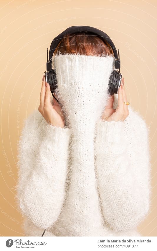 Fun portrait of girl with her trendy white sweater over her head hiding, cold. Listening to music with headphones. Woman with tied hair. Photo in studio. adult