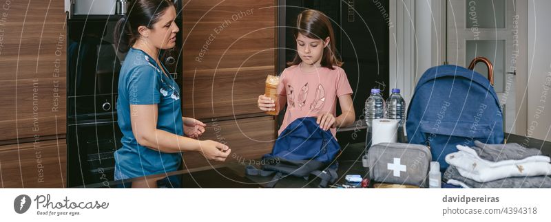 Mother explaining to her daughter how to prepare an emergency ba mother preparing backpack putting cookies helping banner web header panorama panoramic