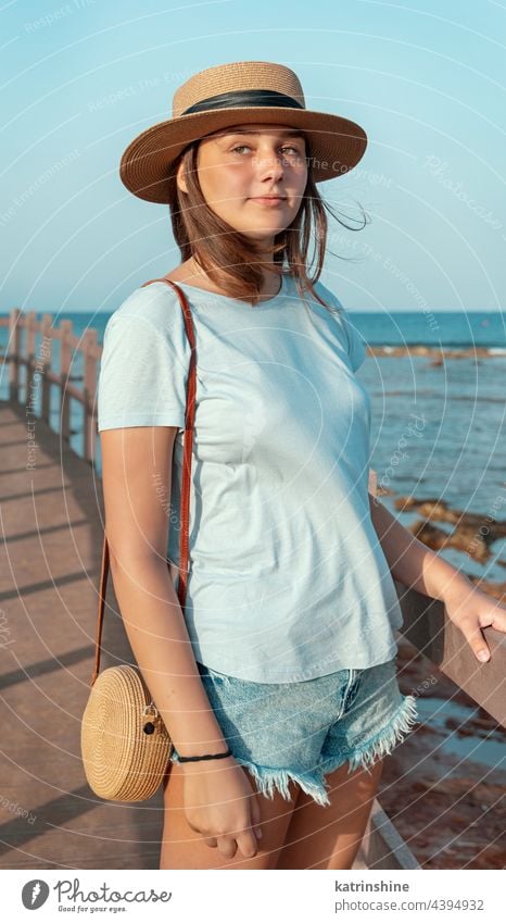Teen girl standing on wooden bridge by the sea sunset teenager adolescent blue mockup Caucasian straw hat walkside sidewalk outdoor vacation travel wearing