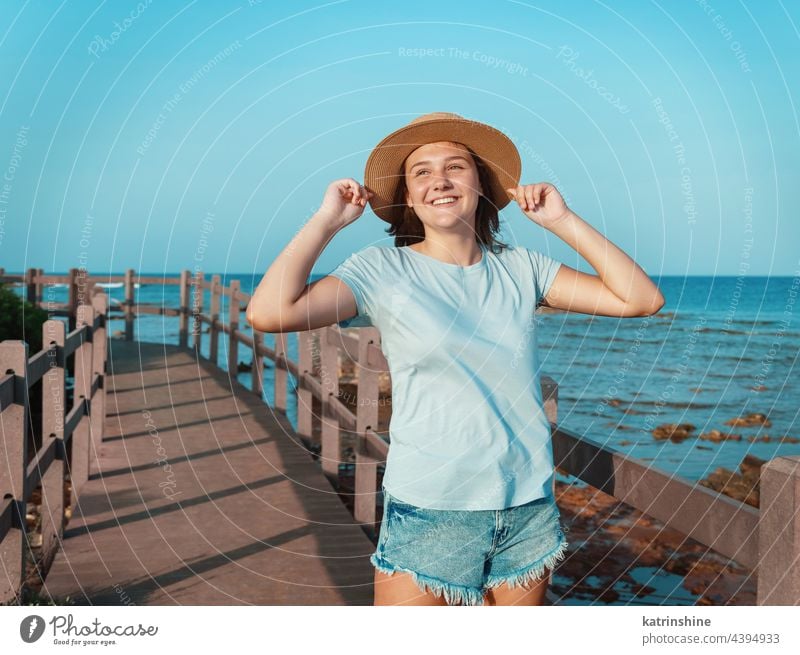 Teen girl standing on wooden bridge by the sea sunset teenager adolescent blue mockup Caucasian straw hat walkside sidewalk outdoor touch vacation travel