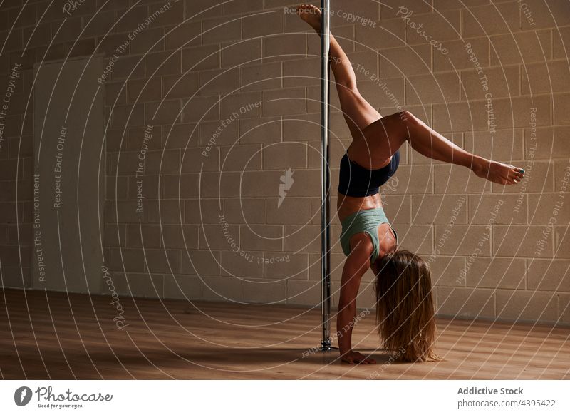 Anonymous female pole dancer performing handstand in studio woman flexible rehearsal grace gymnastic pylon acrobatic handstand bow and arrow upside down