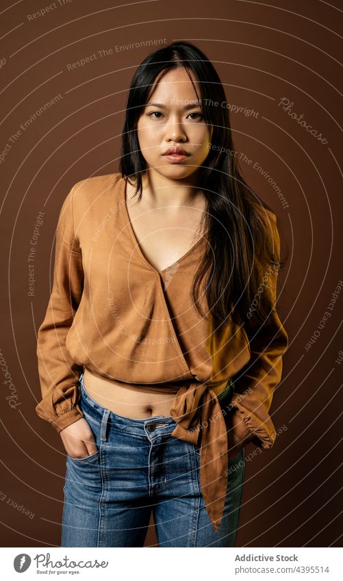 Asian woman in stylish outfit in studio looking at camera style apparel model delight trendy appearance female asian ethnic smile positive jeans young long hair