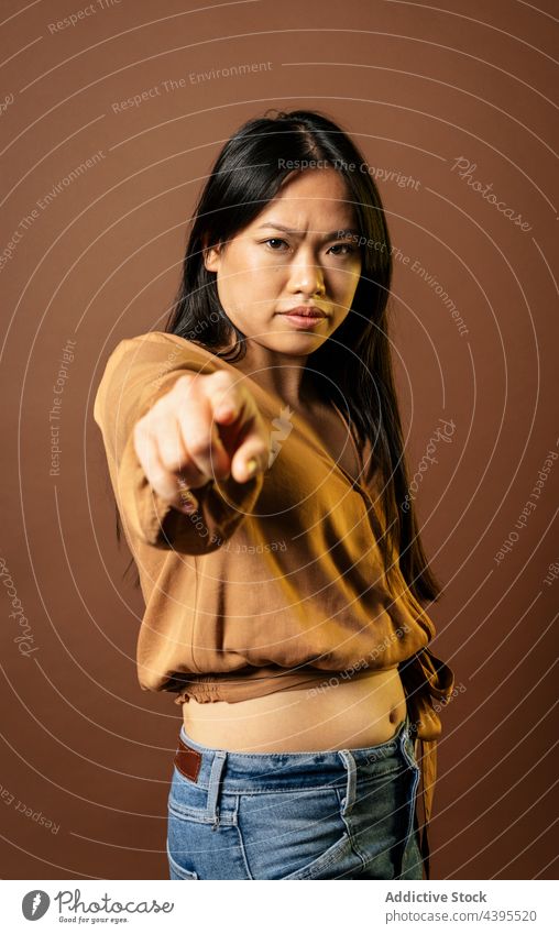 Serious Asian woman pointing at camera point at camera you gesture sign reach out serious frown determine female asian ethnic show index finger forefinger