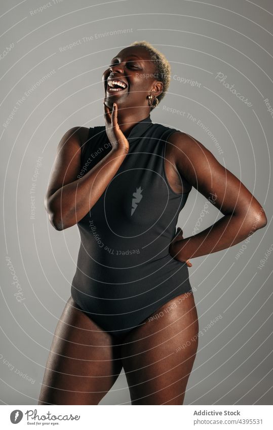 Happy black woman in bodysuit in studio body positive cheerful laugh curve shape delight happy female ethnic african american eyes closed optimist glad content
