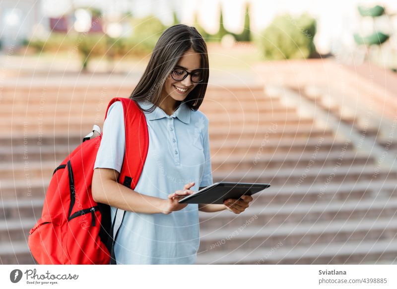 A student girl writes a message on her tablet while walking around the city study backpack stairs glasses smiling studying young outside stylish female