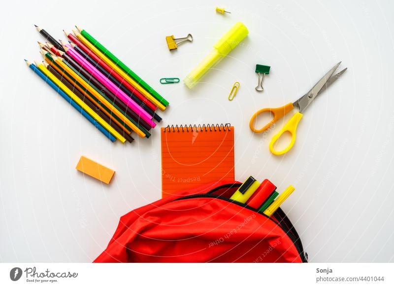 A red school backpack filled with crayons, a pair of scissors and a notepad Schoolbag Red Backpack Education Crayon Claw white background segregated Study