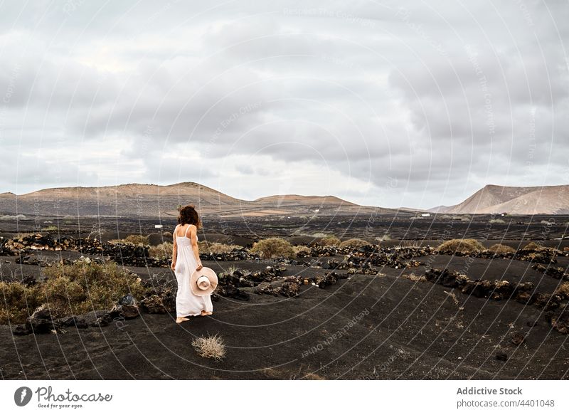 Anonymous female walking in arid valley woman dry travel cloudy sky bush hill explore fuerteventura spain canary islands countryside summer nature rest season