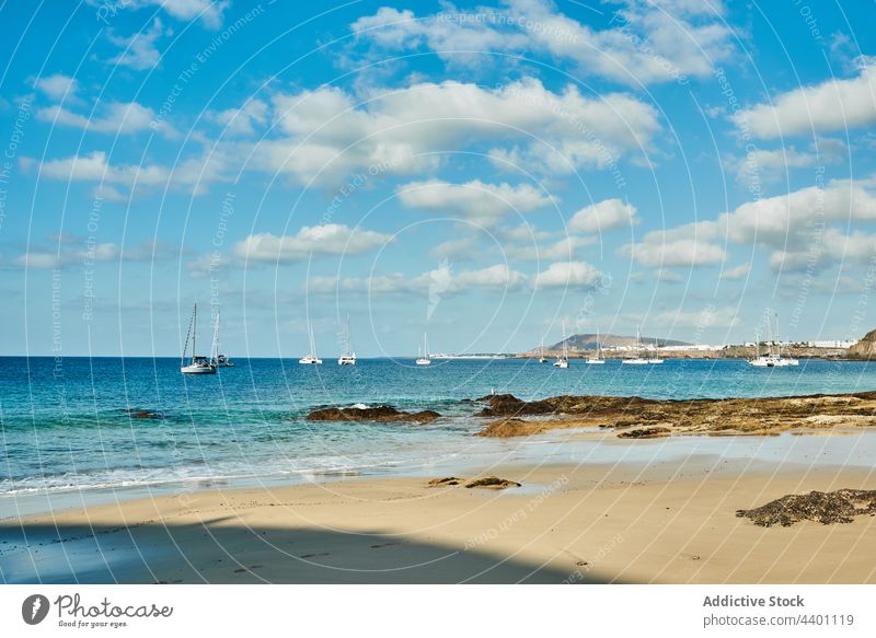Beach with sailboats in the background sea shore summer blue sky water yacht nature rock daytime fuerteventura spain canary islands marine clean turquoise ocean
