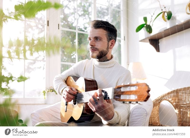 Guitarist playing acoustic guitar in armchair at home guitarist music classic art sound contemplate man string instrument melody dreamy tattoo contemplative