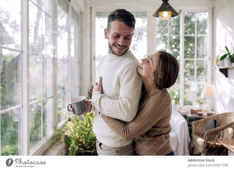 Smiling woman embracing tattooed boyfriend at home couple embrace love relationship romantic contemplate coffee window house cheerful interact mug hot drink
