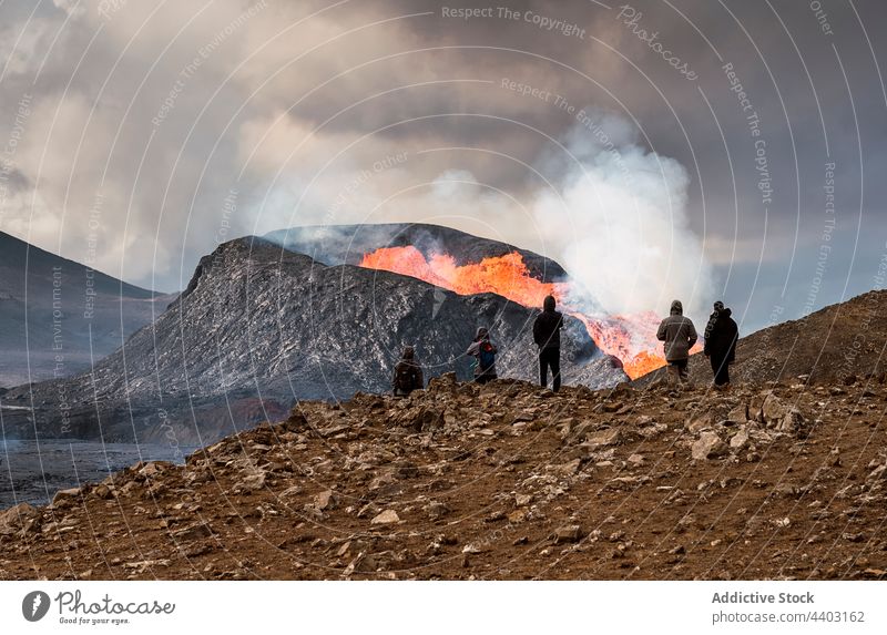 Faceless tourists contemplating active volcano from mountain under cloudy sky admire erupt burn fire nature energy highland fagradalsfjall iceland travel