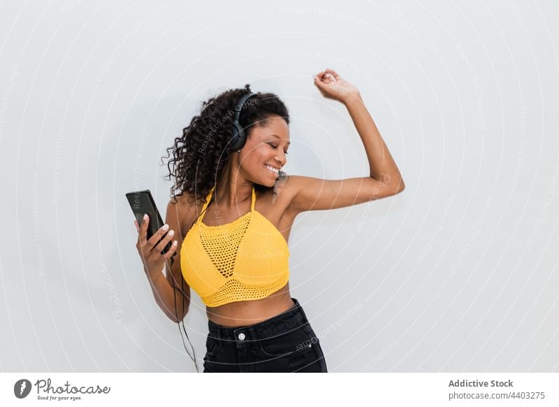 Cheerful black woman in headset with smartphone dancing to music dance headphones listen happy song spare time using gadget device cellphone wire melody