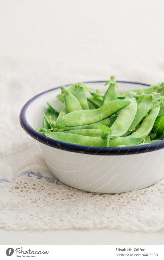 Closeup of sugar snaps peas vegetable bowl food raw green healthy fresh pod natural pods white enamel vintage sugar snap peas uncooked tablecloth lace Vegetable
