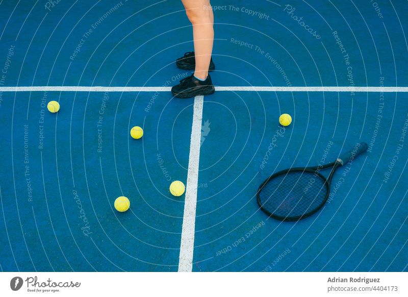 Detail feet of an anonymous woman on a colorful tennis court with racket and tennis balls on it competitions leisure activity recreational sport Court game