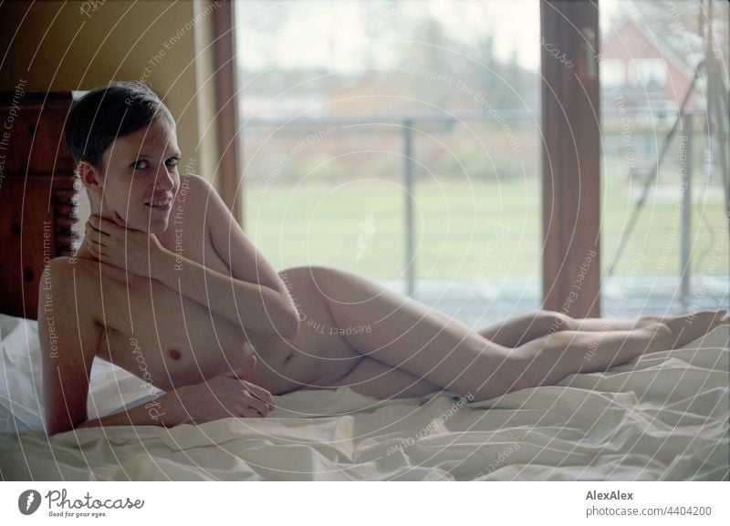 Analogue nude portrait of a young woman on a bed in front of a balcony window Intensive look Expectation emotion Sheets Back-light Expression tripod grain 35mm