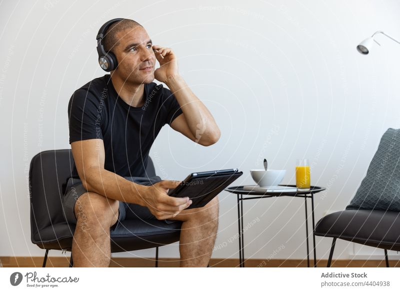 Content man using tablet at home watch video morning male browsing surfing sit connection gadget device internet online headphones content chill entertain