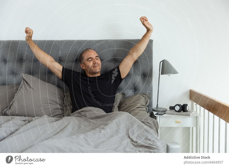Content man stretching on bed after awakening morning bedroom carefree early wake up comfort male enjoy sit soft cozy home peaceful eyes closed content smile