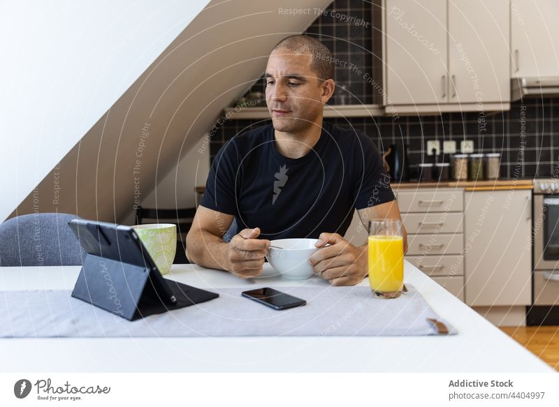 Man browsing tablet during breakfast at home man using morning food surfing online male gadget internet watch kitchen device sit connection beverage drink meal