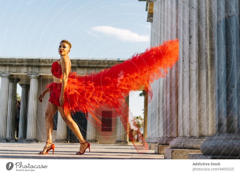 Fashionable black woman in flying dress walking on street fashion style individuality cool self confident portrait colonnade old modern red dress makeup haircut
