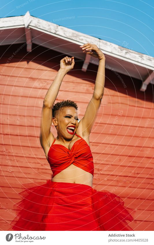 Excited black woman in red dress dancing and screaming dance arms raised fashion style energy excited having fun makeup individuality cool haircut wall house
