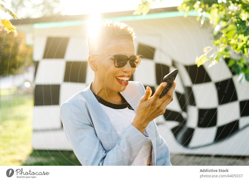 Cheerful black woman with smartphone talking on video call cheerful fashion sunglasses free time park using gadget internet device video chat conversation