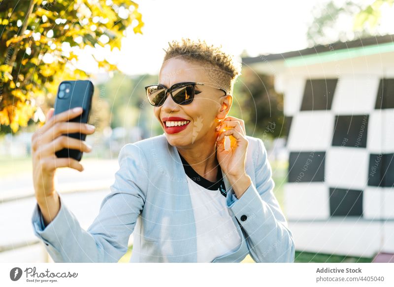 Cheerful black woman with smartphone talking on video call cheerful fashion sunglasses free time park using gadget internet device video chat conversation