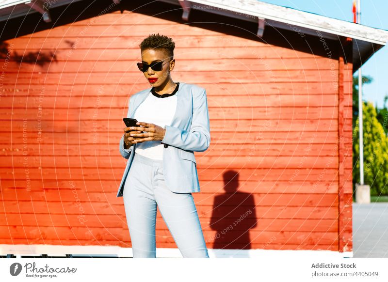 Stylish black woman in sunglasses using smartphone on street fashion stylish individuality cool gadget device style pavement cellphone free time phone call talk
