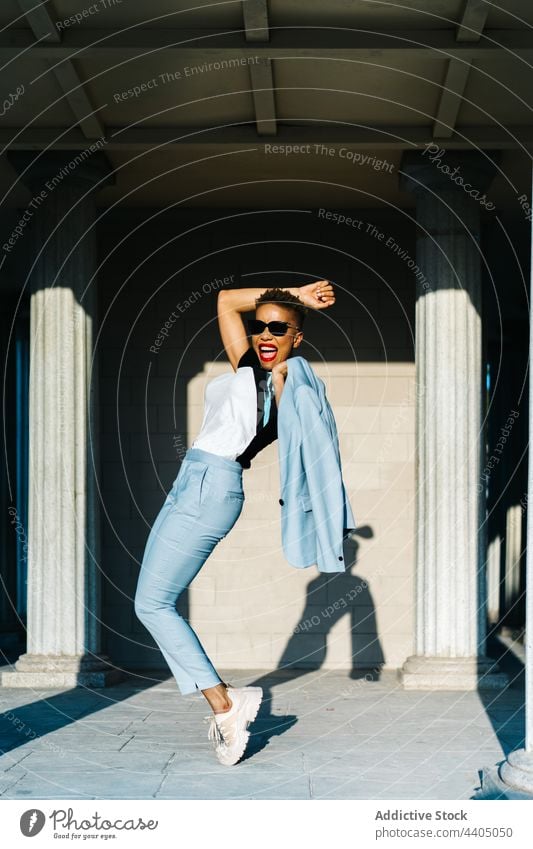 Happy black woman in trendy clothes on tiptoes in town fashion style having fun individuality sunglasses energy happy pavement stylish stand mouth opened
